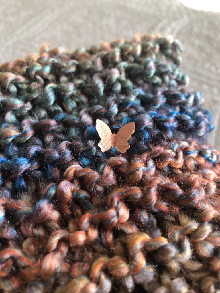 piece of knitting close up with a copper butterfly charm