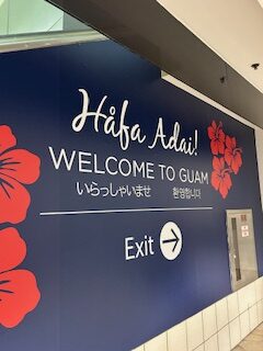 A sign reading Hafa Adai Welcome to Guam with flowers