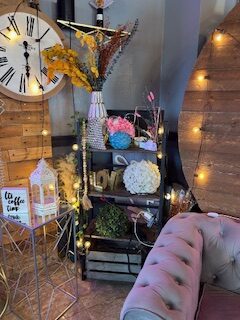 interior of a coffee shop with floral arrangements, a blue couch, a clock with Roman numerals, a tray stand and twinkle lights.