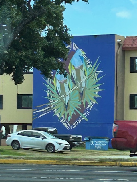 A large building mural with an oblong picture of two tropical birds perches amidst leaves. 