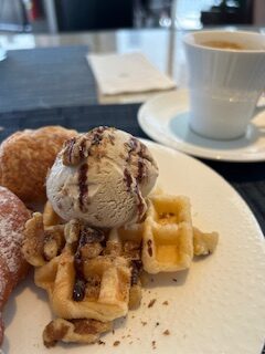 Plate of waffle with scoop of ice-cream and chocolate sauce. Coffee cup in the background.