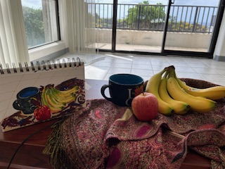 Table with bananas, apple, and mug along with a sketchbook drawing of the same. 