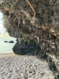 sandy beach overhung by a rocky cliff with ocean and rocks in the background